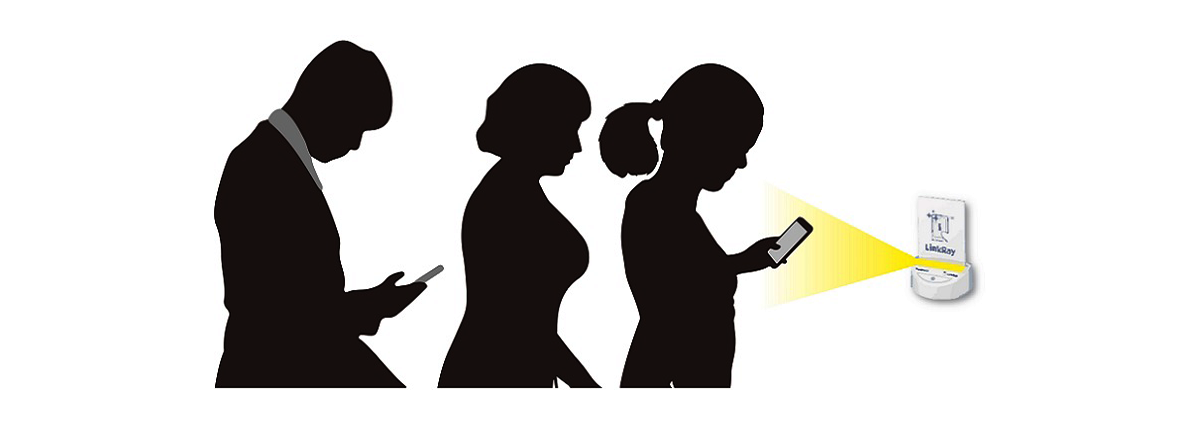 光スタンプ使用イメージ図：三人の人のシルエットがスマホをもってLinkRay対応卓上発信機の前に立っている。一番前に並んいる女性のシルエットが発信機から発せられる光にスマートフォンをかざしている。