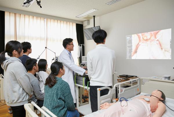 写真：壁に映し出した３D実写映像を確認しながら授業している様子。