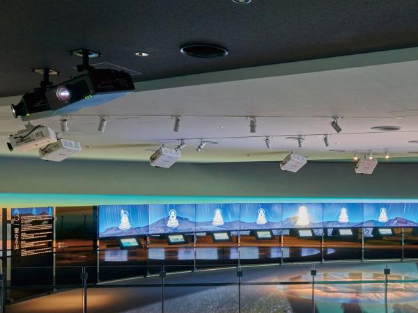写真：展示ゾーンに所狭しと吊られたプロジェクター。天井材の色味に合わせて白色と黒色のキャビネットを使い分けることで、建築との調和が図られている