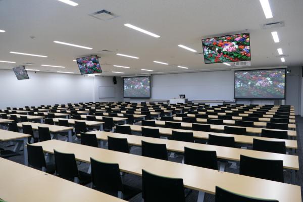 写真：中講義室(202名収容)には計5面のスクリーンとサブディスプレイ