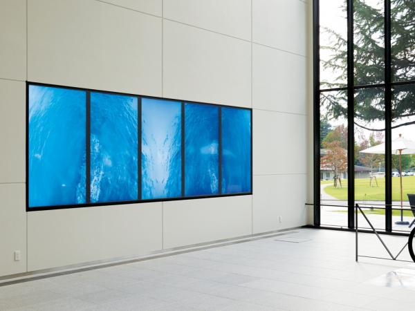 写真：80型の大画面、700 cd/㎡の高輝度を誇るTH-80LF50Jを5面マルチ設置。大開口のガラス張りの吹き抜け空間でも鮮明な映像を表示。造形デザイン学科の作品発表の場や保護者との撮影ポイントになっている