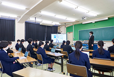 写真：巨大な電子黒板と、一人一台のレッツノートを用いて授業が行われています。