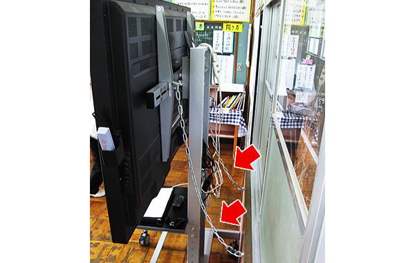 写真：電子黒板が地震などで転倒しないように、使用しないときにはチェーン（赤矢印）で壁に固定している。