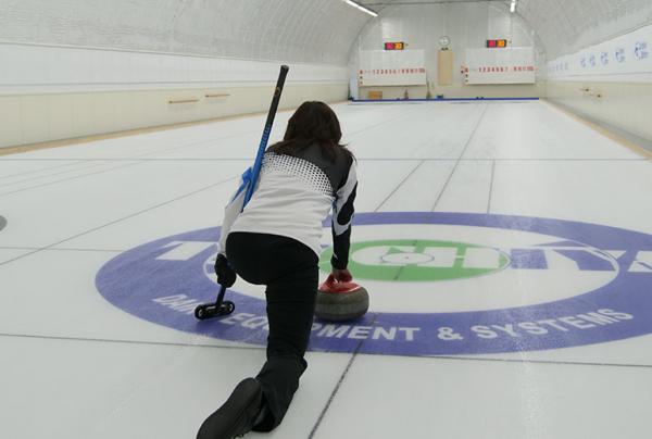 写真：カーリングコートの上で奥のハウスをめがけてストーンをリリースする女性選手