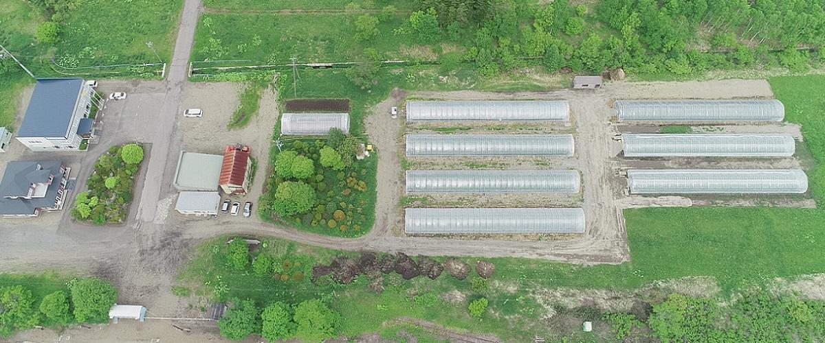 写真：広い敷地に並ぶメロン栽培用のビニールハウスとそれを管理する事務所を上空から撮影した様子