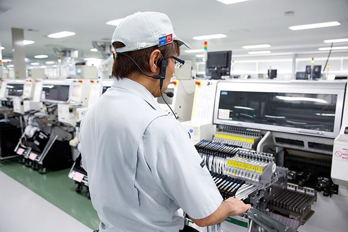 骨伝導ヘッドホンをつけ、生産設備の点検をする工員