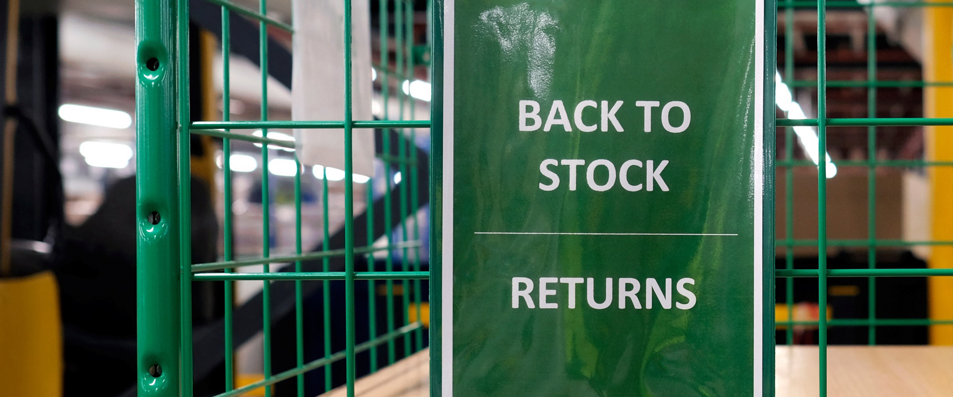 BACK TO STOCK RETURNSのカードがかけられた荷物カートが置かれている倉庫