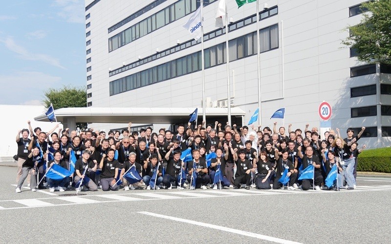 パナソニックの神戸工場の前で大勢の人々が青い旗を持ち、集合している。