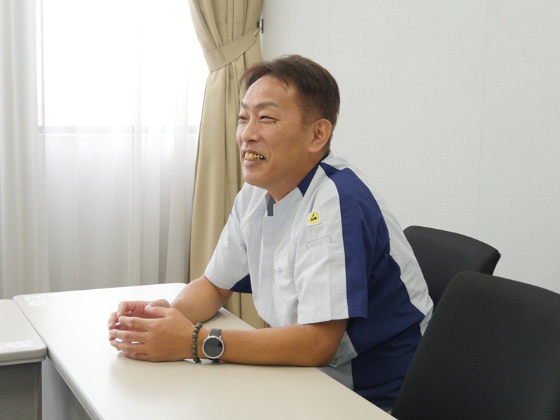 明るい部屋の中で男性が椅子に座り、微笑んでいる。
