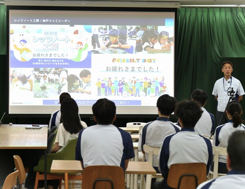 室内でプレゼンテーションを受ける人々。スクリーンにはカラフルなスライドが表示。