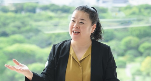 緑豊かな景色を背景に、身ぶりを交えて話す女性