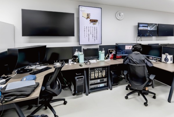 デスクに座る人と複数のモニターが並ぶオフィスの作業スペース。