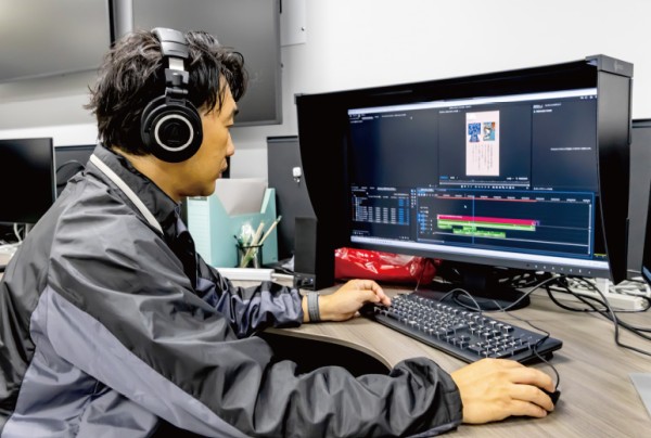 ヘッドホンを着けた男性がコンピューター画面で編集作業をしている。