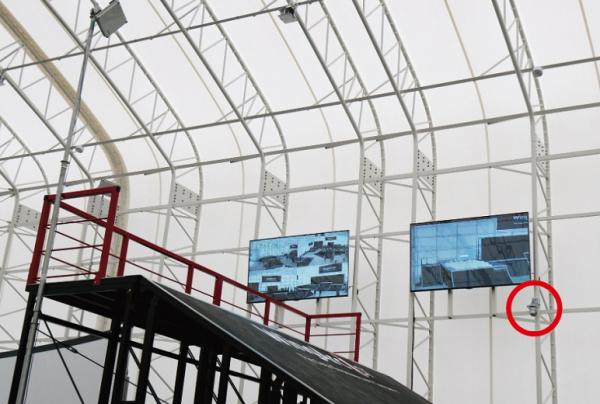 写真：スタート台付近の様子。スタート台脇にある壁に2台の大きなスクリーンが設置されている。その下方にスタート台をとらえるように設置されたネットワークカメラ。