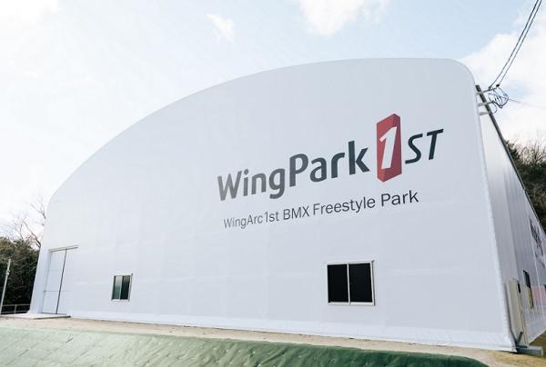 写真：WingPark1st 外観の様子。白いドーム型の建物の壁面に大きく「WingPark1st」のロゴが描かれている。