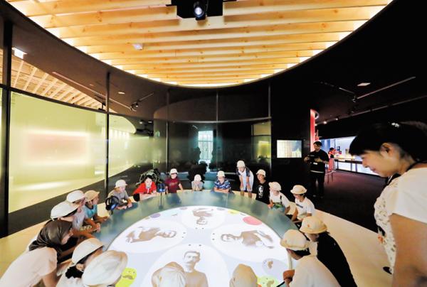 写真：イントロダクションスペースに映し出された映像。天井からテーブルに向けて投影されており、それを子供たちが熱心に見ている様子。