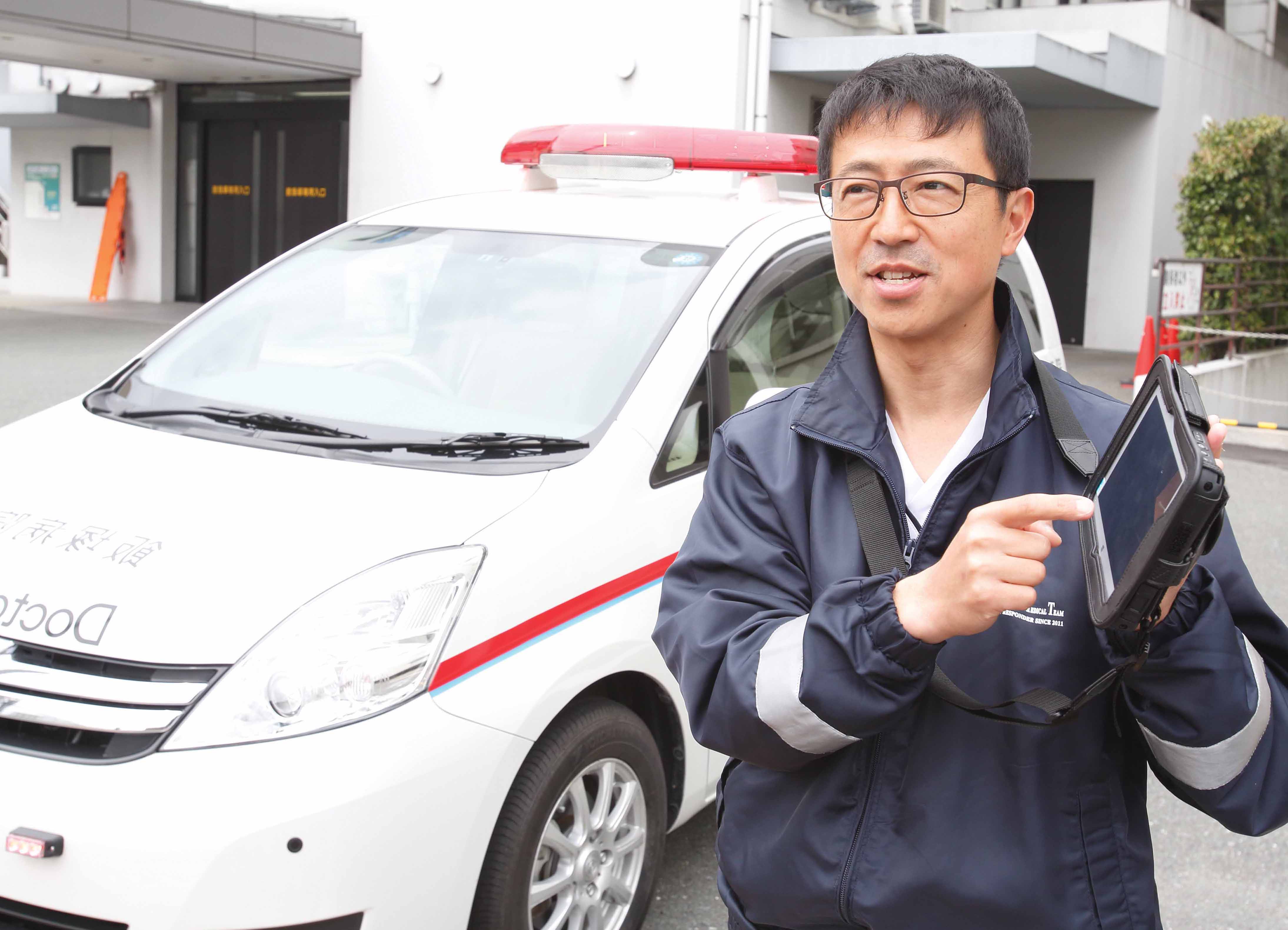 写真:ドクターカーの前でTOUGHPADを操作する都留 和宏 様