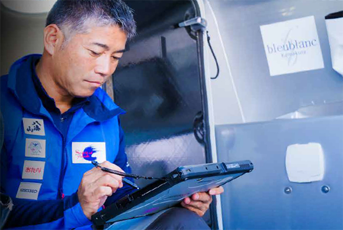 写真：タブレット部分を取り外し甲板で作業をする白石さん