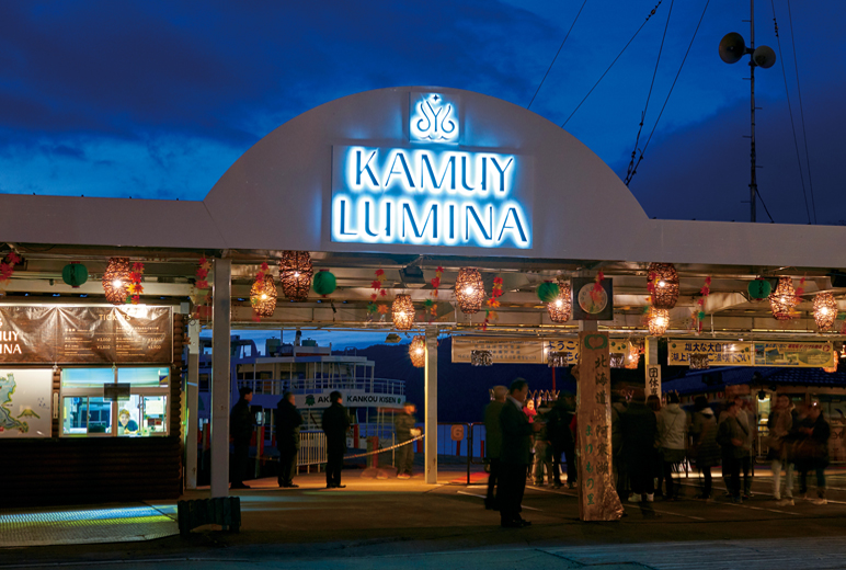 写真：日が暗くなり発着所のゲートの『KAMUY LUMINA』部分が点灯する様子。