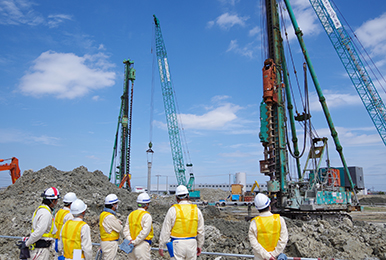写真：杭基礎工事の現場。作業している人々の様子。