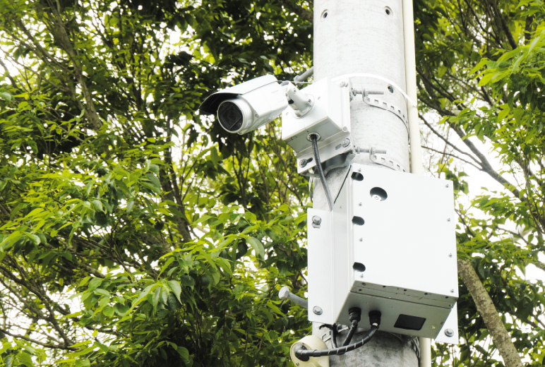 写真：電柱上部に設置されたた防犯カメラシステムとネットワークカメラ用60 GHz通信BOX。