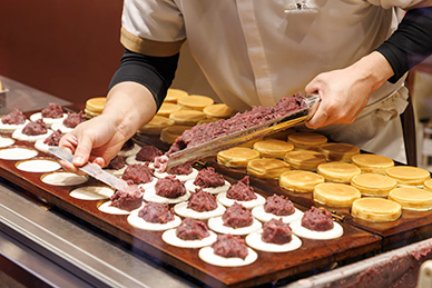 御座候様では、⽣地の製造から焼き上げまでを各店舗で⾏い、できたての商品をその場でお客様に提供。